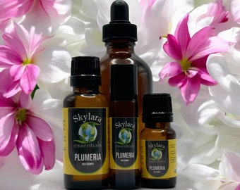 Könnte beinhalten: Drei Braunglasflaschen mit Skylara Essentials Plumeria Nag Champa Öl, bestehend aus einer großen Pipettenflasche, einer mittleren Roll-on-Flasche und einer kleinen ätherischen Ölflasche, alle mit gelben Etiketten und Text, vor weiß-rosa Blüten.