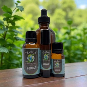 May include: Four amber glass bottles of essential oil products. The bottles have black caps and labels that read "Skylara essentials ARMOISE". The background is a blurred view of green foliage.