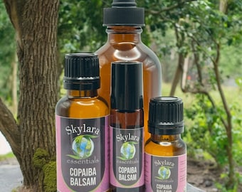 Könnte beinhalten: Verschiedene braune Glasflaschen mit schwarzen Deckeln und Etiketten. Die Etiketten tragen die Aufschrift "Skylara essentials COPAIBA BALSAM" mit einer Weltkugel-Grafik. Eine Tropfflasche ist im Hintergrund zu sehen. Die Flaschen stehen auf einer natürlichen Oberfläche mit einem Baumstamm im Hintergrund.
