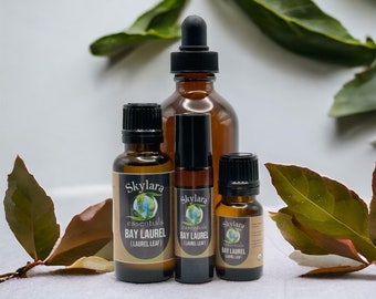 May include: Four amber glass bottles of essential oils, labeled "Skylara essentials BAY LAUREL (LAUREL LEAF)". The bottles vary in size, with black caps and a dropper. Green leaves and a white background complete the image.