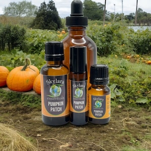 May include: Three amber glass bottles of Skylara Essentials Pumpkin Patch oil. The largest bottle has a black dropper cap, the middle bottle is a rollerball, and the smallest has a black screw cap. Each features a label with a globe logo.