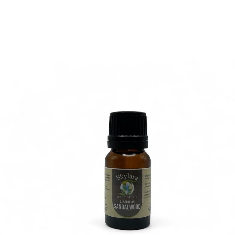 Puede incluir: Una peque&ntilde;a botella de vidrio &aacute;mbar de aceite esencial de s&aacute;ndalo australiano Skylar essentials. La botella tiene una tapa negra y una etiqueta con el nombre de la marca y la informaci&oacute;n del producto. El fondo es blanco.