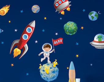 Pode incluir: Uma parede azul com adesivos de parede com tema espacial. Os adesivos incluem um foguete, planetas, estrelas, um astronauta, um OVNI e um cometa. O astronauta está em pé em um planeta e segurando uma bandeira que diz "ALEX".