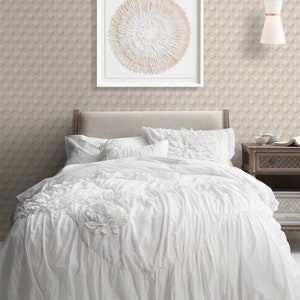 K&ouml;nnte beinhalten: Wei&szlig;er, ger&uuml;schter Bettbezug mit einem wei&szlig;en Kopfteil und zwei wei&szlig;en Kissen. &Uuml;ber dem Bett h&auml;ngt ein gerahmtes, rundes Wandbild mit einem wei&szlig;en und beigefarbenen Federdesign.