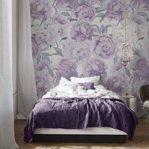May include: A bedroom with a bed with a purple duvet and white pillows. The wall behind the bed is covered in a wallpaper with a floral pattern of purple peonies.