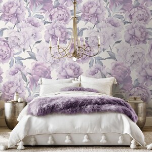 May include: A white bed with a purple faux fur throw blanket and white pom-pom trim. The bed is in front of a wall with a floral wallpaper featuring large purple peonies.