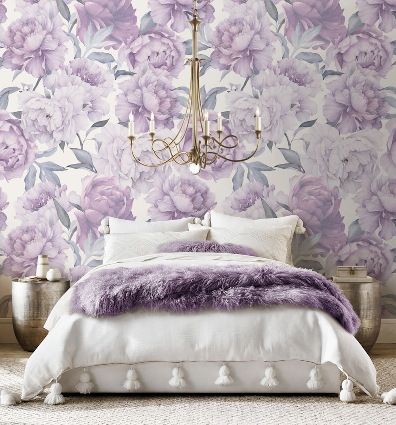 May include: A white bed with a purple faux fur throw blanket and white pom-pom trim. The bed is in front of a wall with a floral wallpaper featuring large purple peonies.