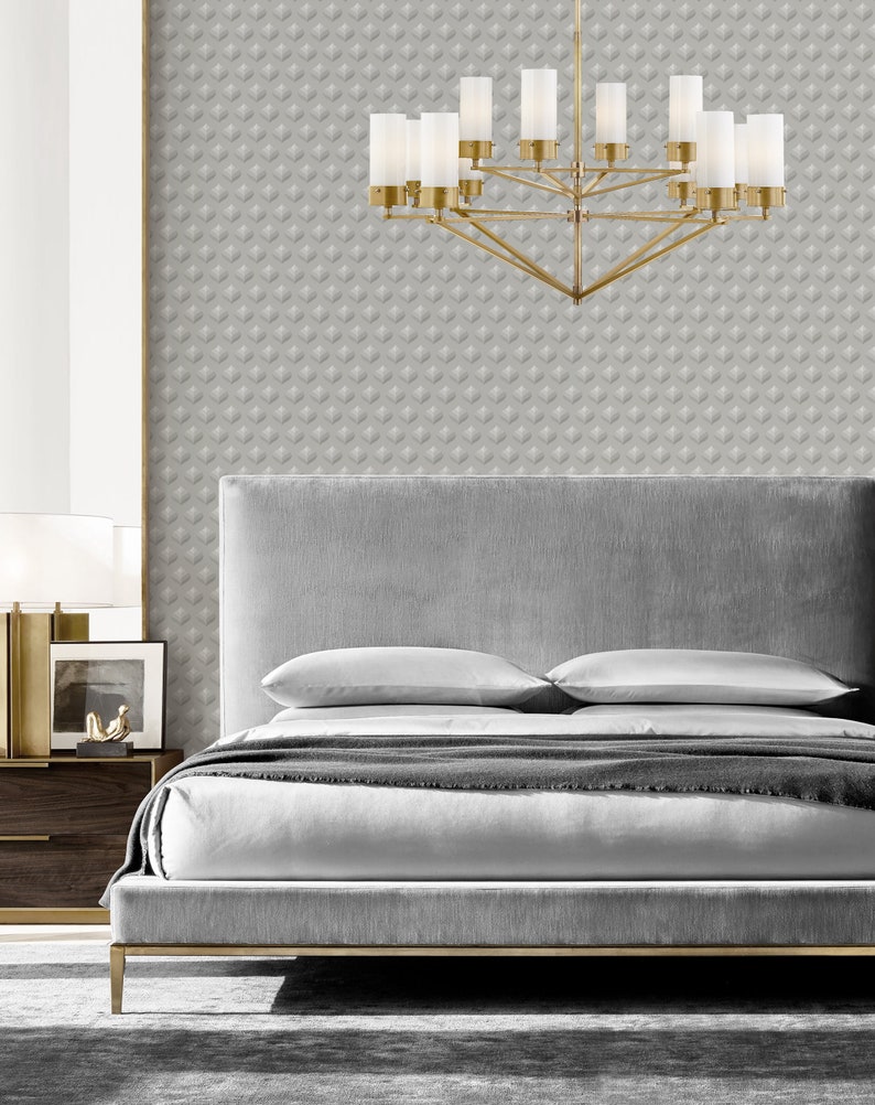 K&ouml;nnte beinhalten: Ein graues, gepolstertes Bettgestell mit einem goldenen Metallfu&szlig; und zwei wei&szlig;en Kissen. Das Bett steht in einem Schlafzimmer mit grauer, gemusterter Tapete und einem goldenen Kronleuchter mit mattierten Glasschirmen.