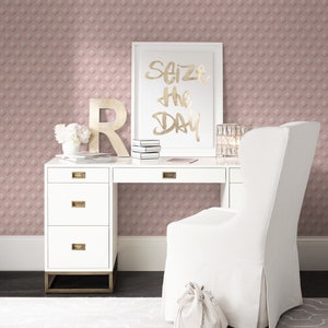 K&ouml;nnte beinhalten: Ein wei&szlig;er Schreibtisch mit goldenen Akzenten und vier Schubladen. Ein wei&szlig;er Stuhl mit einer wei&szlig;en Tasche auf dem Boden davor. Ein gerahmter Druck mit dem Text "Seize the Day" in goldenen Buchstaben befindet sich auf dem Schreibtisch. Die Wand hinter dem Schreibtisch ist mit einer rosa Tapete mit geometrischem Muster bedeckt.