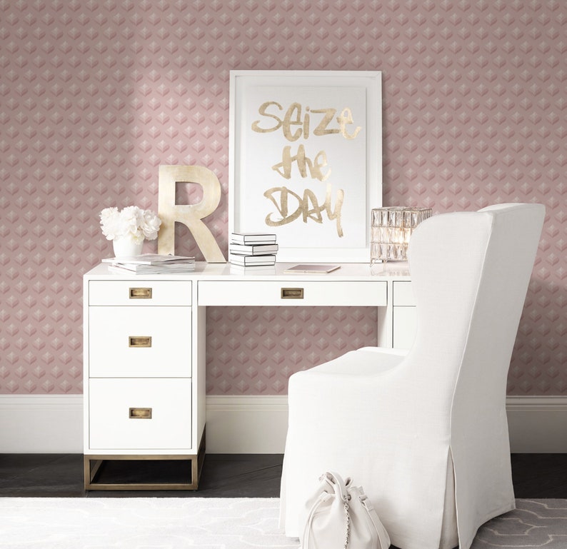 K&ouml;nnte beinhalten: Ein wei&szlig;er Schreibtisch mit goldenen Akzenten und vier Schubladen. Ein wei&szlig;er Stuhl mit einer wei&szlig;en Tasche auf dem Boden davor. Ein gerahmter Druck mit dem Text "Seize the Day" in goldenen Buchstaben befindet sich auf dem Schreibtisch. Die Wand hinter dem Schreibtisch ist mit einer rosa Tapete mit geometrischem Muster bedeckt.