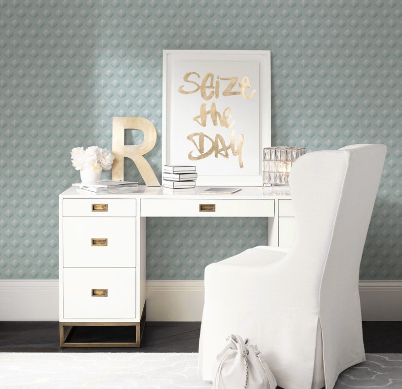 K&ouml;nnte beinhalten: Wei&szlig;er Schreibtisch mit vier Schubladen und goldenen Beschl&auml;gen. Ein wei&szlig;er Stuhl mit einer wei&szlig;en Tasche auf der Sitzfl&auml;che. Ein gerahmter Druck mit dem Text "Seize the Day" in goldenen Buchstaben. Die Wand hinter dem Schreibtisch ist mit einer hellblauen Tapete mit geometrischem Muster bedeckt.