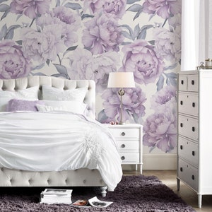 May include: A white upholstered bed with a tufted headboard and a white nightstand with three drawers. The bed is dressed in white bedding and a lavender throw pillow. The wall behind the bed is covered in a floral wallpaper with large purple peonies.