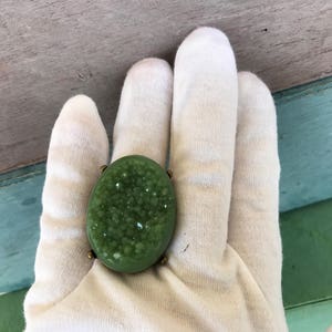May include: A green oval-shaped ring with a textured surface. The ring is set in a brass setting.