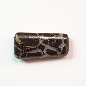 May include: A rectangular, polished gemstone with a dark brown base color and a network of iridescent, light blue and green veins. The stone has rounded edges and a smooth, reflective surface, showcasing natural patterns.