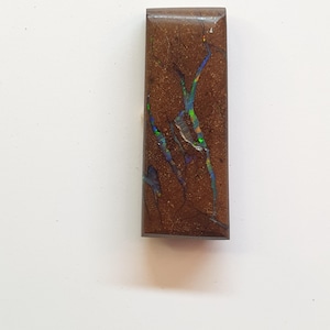 May include: A rectangular, polished gemstone with a rich brown base color. The stone features intricate, vein-like patterns in shades of blue, green, and yellow, creating a striking contrast. The gemstone is likely used for jewelry or decorative purposes.