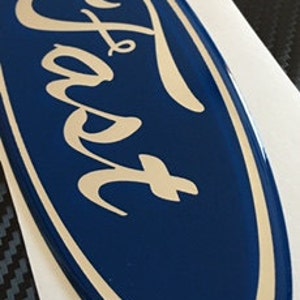 May include: A blue oval-shaped emblem with the word "Ford" in a silver script font.