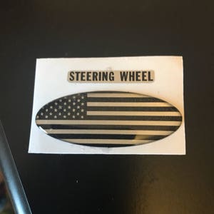 May include: A black and white American flag sticker with the words "Steering Wheel" printed above it.