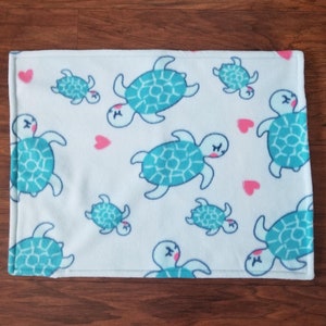 May include: A white fleece blanket with a repeating pattern of blue sea turtles and pink hearts.
