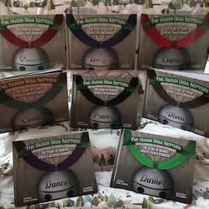 May include: A set of eight children's books about Santa's reindeer. Each book features a different reindeer with a silver bell and a colourful background. The titles of the books are "The Sleigh Bell Letters" and the name of the reindeer. The books are arranged in two rows of four.