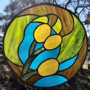 May include: A round stained glass window with a blue, green, and yellow design. The design features three yellow flowers with green stems and leaves.