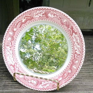 May include: A pink and white ceramic plate with a mirror in the center. The plate has a pink and white acorn design around the edge.