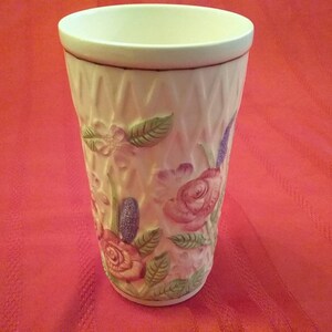 May include: A white ceramic vase with a floral design. The vase has a textured surface and features pink, purple, and green flowers.