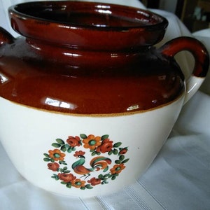 May include: A brown and white ceramic crock with a rooster and floral design. The crock has two handles and a wide opening.