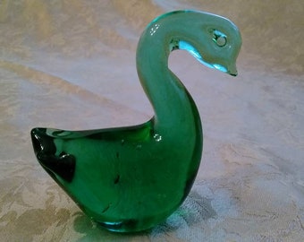 May include: A green glass swan figurine with a long neck and a curved beak. The swan is sitting on a white surface.