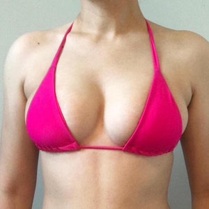 May include: A vibrant pink bikini top with a halter neck. The top has a triangle cup design and is made from a smooth fabric. The bikini top is a bright, eye-catching shade of pink.