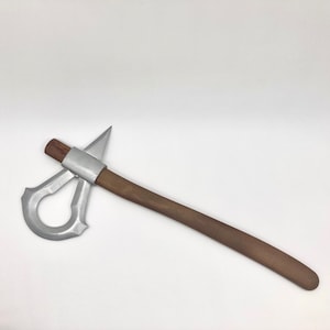 Może przedstawiać: Srebrna tomahawk z drewnianym trzonkiem. Głowa tomahawka ma kształt łzy z otworem w środku.