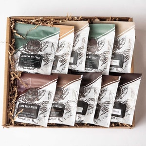 May include: A gift box filled with various coffee bean bags. The bags have a white background with a leaf design and text. The box is brown and filled with shredded paper. The coffee bags have different colors and text labels.
