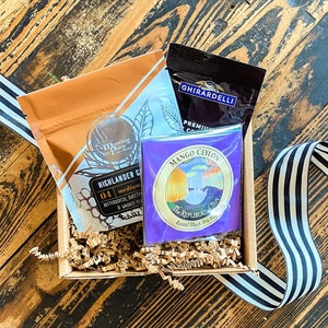 K&ouml;nnte beinhalten: Ein Geschenkkorb gef&uuml;llt mit braunem Seidenpapier, der einen Beutel Highlander Grocer Tee, eine Schachtel Ghirardelli Schokolade und eine Schachtel Mango Ceylon Tee von The Republic of Tea enth&auml;lt.