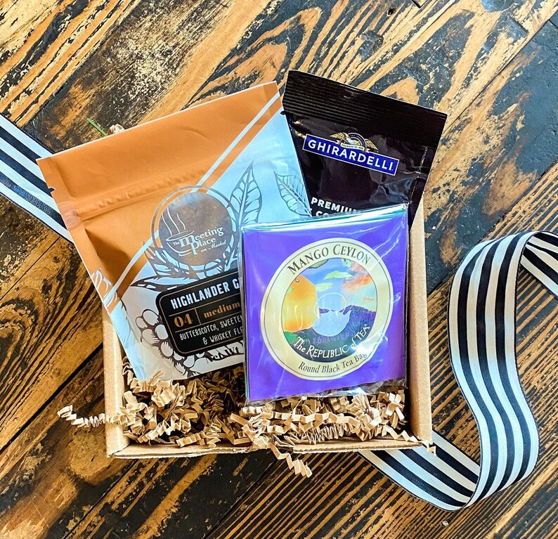 K&ouml;nnte beinhalten: Ein Geschenkkorb gef&uuml;llt mit braunem Seidenpapier, der einen Beutel Highlander Grocer Tee, eine Schachtel Ghirardelli Schokolade und eine Schachtel Mango Ceylon Tee von The Republic of Tea enth&auml;lt.