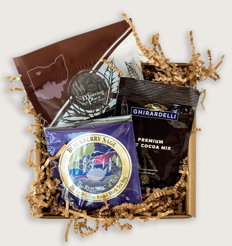 K&ouml;nnte beinhalten: Eine braune Geschenkbox, gef&uuml;llt mit braunen Papierschnitzeln, enth&auml;lt einen braunen Teebeutel mit dem Text "Blackberry Sage" und den Worten "The Republic of Tea" in einem Kreis, ein braunes P&auml;ckchen mit hei&szlig;er Schokolade mit dem Text "Ghirardelli Premium Hot Cocoa Mix" und einen braunen Teebeutel mit dem Text "The Meeting Place" in einem Kreis.