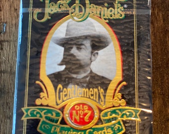 May include: A black and gold deck of playing cards featuring a portrait of Jack Daniel in a black and white photo. The text on the box reads "Jack Daniel's Old No. 7 Gentlemen's Playing Cards".