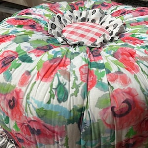 May include: A round, white floral patterned ottoman with a red and white gingham center and a black and white polka dot trim.