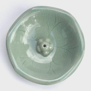May include: A celadon green ceramic incense holder with a lotus leaf design. The holder has a central flower-shaped incense stick holder and a crackle glaze finish. The dish is approximately 4 inches in diameter.