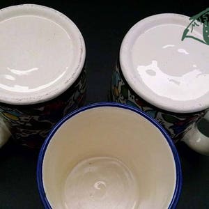 May include: Three ceramic mugs with white interiors and handles. The mugs have colorful floral patterns and a blue rim. The image includes the text "MYSTIC LAND PAINTED OWNA ADOBE".