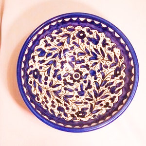 Op de afbeelding: Een ronde keramische kom met een diepblauwe rand en een wit interieur. De kom is versierd met een bloemmotief in blauw en bruin. Het ontwerp toont gestileerde bladeren en bloemen, waardoor een decoratief en artistiek stuk ontstaat.