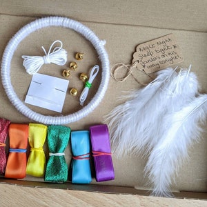 May include: A craft kit in a cardboard box, featuring a white yarn-wrapped hoop, white feathers, colorful ribbons, gold bells, and a tag that reads "Night Night Sleep tight, Santa's on his way tonight!"