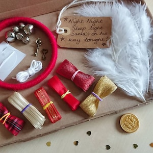 May include: A festive Christmas Eve box filled with holiday-themed items. Includes a red wrapped circle with bells, keys, ribbons, a feather, and a tag that reads "Night Night Sleep tight Santa's on his way tonight!"