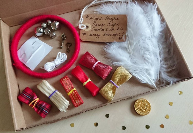 May include: A festive Christmas Eve box filled with holiday-themed items. Includes a red wrapped circle with bells, keys, ribbons, a feather, and a tag that reads "Night Night Sleep tight Santa's on his way tonight!"