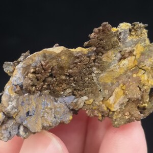 Pu&ograve; includere: Primo piano di una roccia ruvida di forma irregolare con una miscela di colori marroni, gialli e blu. La roccia ha una superficie stratificata e testurizzata.