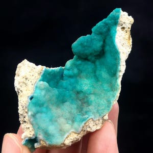 May include: A teal blue mineral specimen with a rough, white exterior. The mineral is a geode, with a hollow interior lined with crystals.