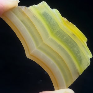 May include: A yellow, green, and white agate slice with a curved shape and banded pattern.