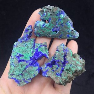 Peut inclure: Trois spécimens de minéraux bruts d'azurite et de malachite naturelle. Les spécimens sont de couleur bleu foncé et verte avec une texture rugueuse et irrégulière.