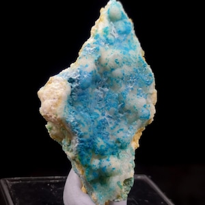 Puede incluir: Un vibrante espécimen mineral con una llamativa combinación de colores. La pieza muestra un tono turquesa brillante intercalado con blanco cremoso y toques de amarillo. La forma general es irregular, con una superficie rugosa y texturizada.