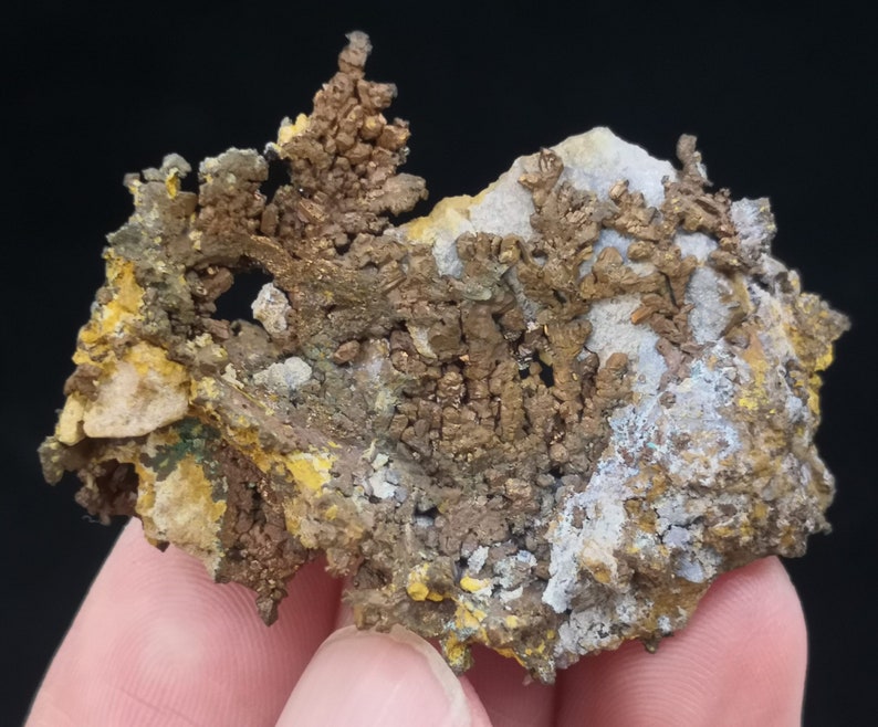 Pu&ograve; includere: Un ammasso di cristalli di rame con una superficie ruvida e testurizzata. I cristalli sono di un colore marrone rossiccio intenso e hanno un bagliore metallico. L'ammasso &egrave; circondato da una matrice di roccia bianca e grigia.