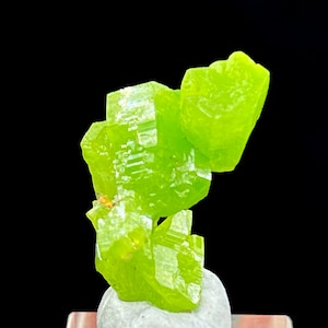 May include: Bright green crystal cluster with a geometric structure. The crystals are a vibrant, lime green color and appear to be translucent. The mineral specimen is set against a black background.