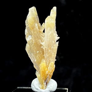May include: A natural, light yellow crystal cluster with a spiky, layered structure. The crystal sits on a small, white, rounded base, with a dark background. The crystal has a rough, textured surface and varying shades of yellow.